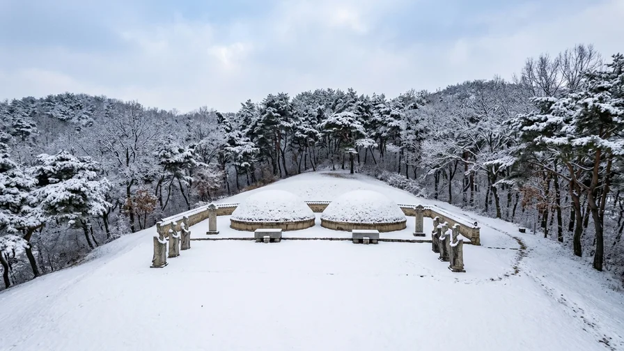 Snow-covered Joseon royal tomb burial mounds and stone figures side by side on a hill